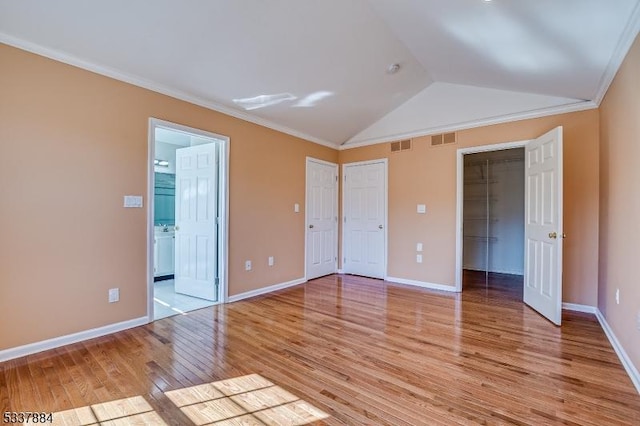 unfurnished bedroom featuring visible vents, crown molding, baseboards, vaulted ceiling, and light wood-style flooring