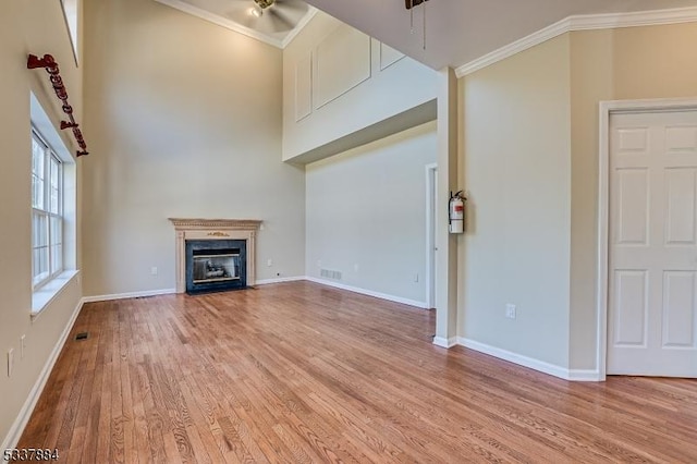 unfurnished living room with a glass covered fireplace, wood finished floors, baseboards, and ornamental molding