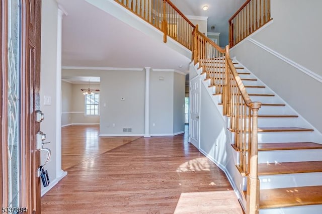 foyer entrance with ornamental molding, wood finished floors, a high ceiling, baseboards, and stairs