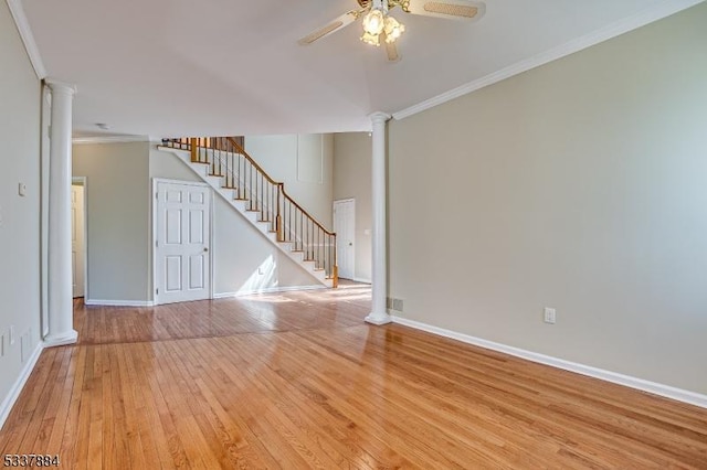 empty room with crown molding, light wood finished floors, ceiling fan, stairs, and ornate columns