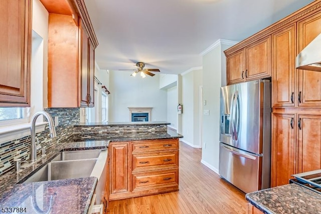 kitchen featuring dark stone countertops, stainless steel fridge with ice dispenser, a sink, decorative backsplash, and wall chimney range hood