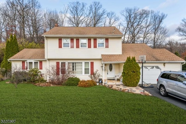 colonial-style house featuring a garage, a shingled roof, driveway, a chimney, and a front yard