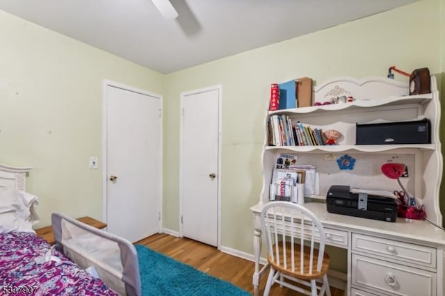 bedroom with ceiling fan, light wood finished floors, built in study area, and baseboards