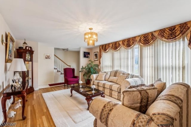 living area featuring a notable chandelier, light wood-style flooring, baseboards, and stairs