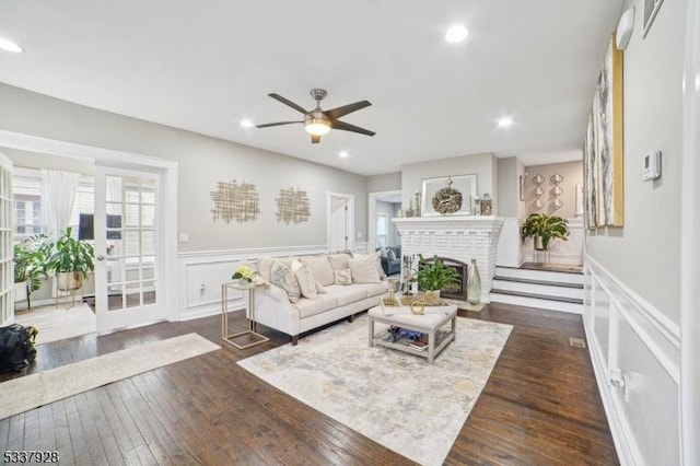 living area featuring a brick fireplace, recessed lighting, dark wood-style flooring, and a wainscoted wall