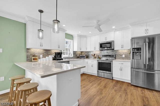 kitchen featuring stainless steel appliances, kitchen peninsula, hanging light fixtures, and white cabinets