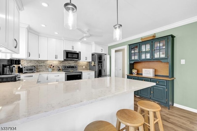 kitchen featuring stainless steel appliances, white cabinetry, kitchen peninsula, and decorative light fixtures