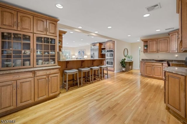 kitchen with open shelves, visible vents, appliances with stainless steel finishes, a peninsula, and a kitchen bar