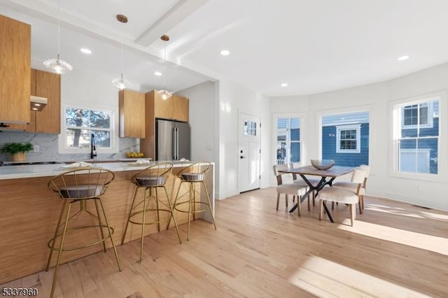 kitchen featuring light countertops, hanging light fixtures, freestanding refrigerator, modern cabinets, and a kitchen bar