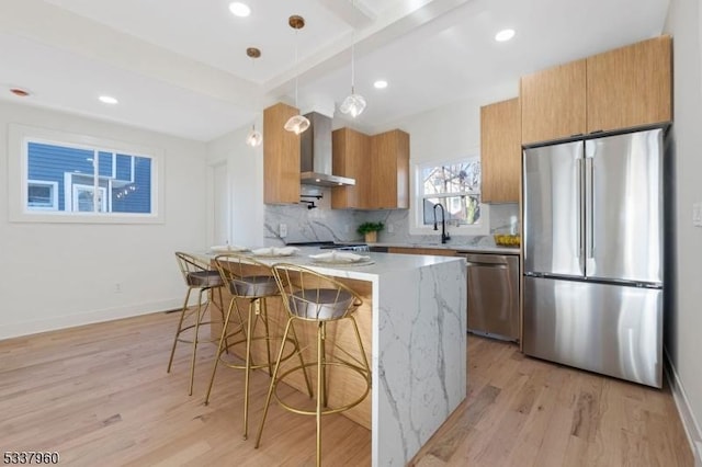 kitchen featuring a breakfast bar, decorative light fixtures, light stone countertops, stainless steel appliances, and wall chimney range hood