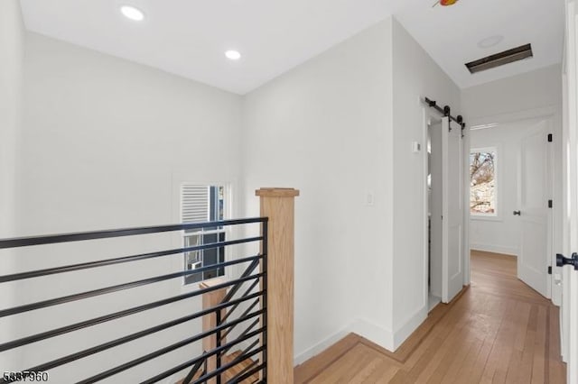 corridor with light wood-type flooring, a barn door, baseboards, and recessed lighting