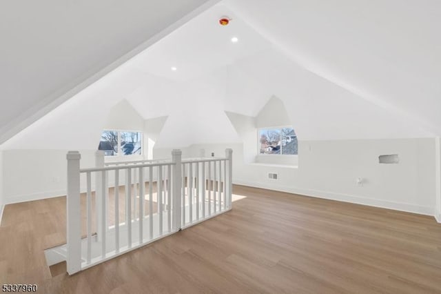 bonus room featuring light wood-type flooring, visible vents, vaulted ceiling, and baseboards