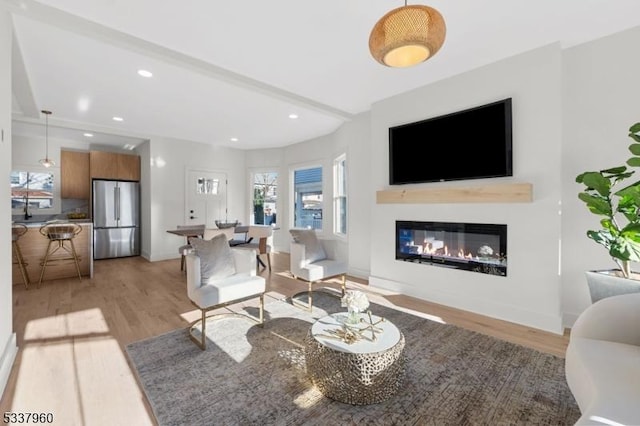 living area featuring baseboards, light wood finished floors, a glass covered fireplace, and recessed lighting