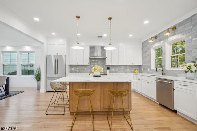 kitchen with white cabinets, stainless steel appliances, a kitchen island, and wall chimney range hood