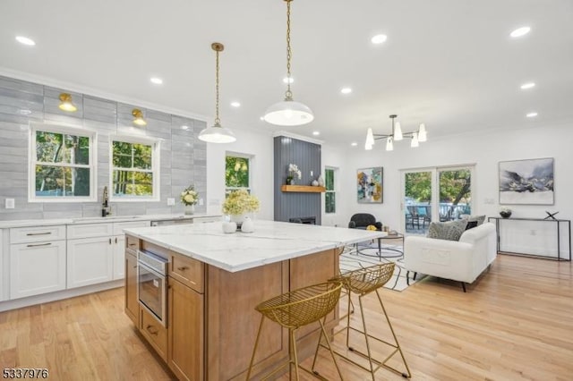 kitchen featuring sink, white cabinets, ornamental molding, a center island, and light stone counters