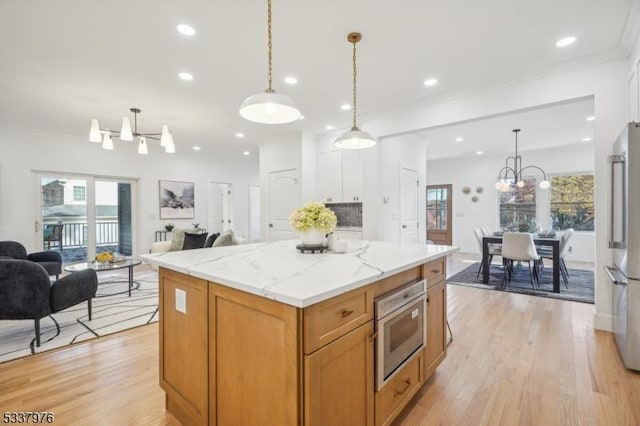 kitchen featuring an inviting chandelier, decorative light fixtures, a center island, light hardwood / wood-style flooring, and light stone countertops