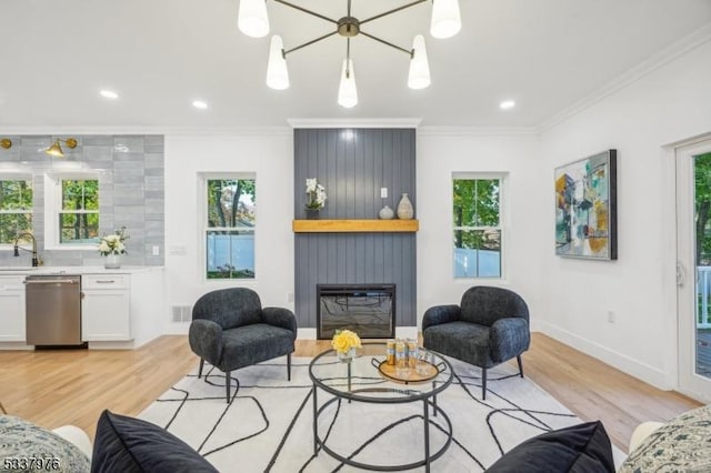 living room featuring crown molding, a large fireplace, sink, and light wood-type flooring