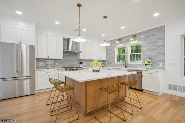 kitchen featuring white cabinetry, wall chimney range hood, a kitchen island, and appliances with stainless steel finishes