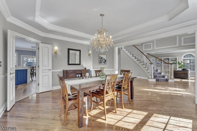 dining space with stairs, a tray ceiling, wood finished floors, and ornamental molding