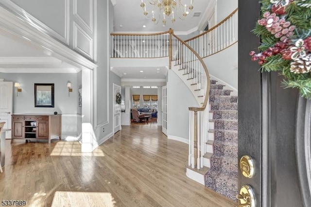 entryway featuring crown molding, a chandelier, stairs, a high ceiling, and light wood-style floors