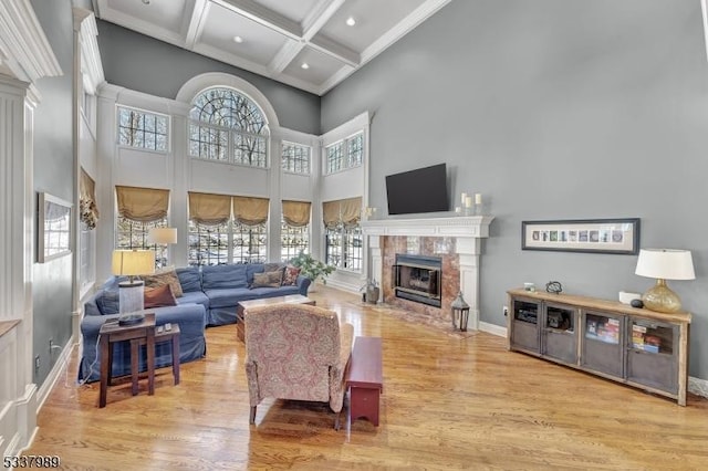 living area with a tiled fireplace, coffered ceiling, wood finished floors, baseboards, and a towering ceiling