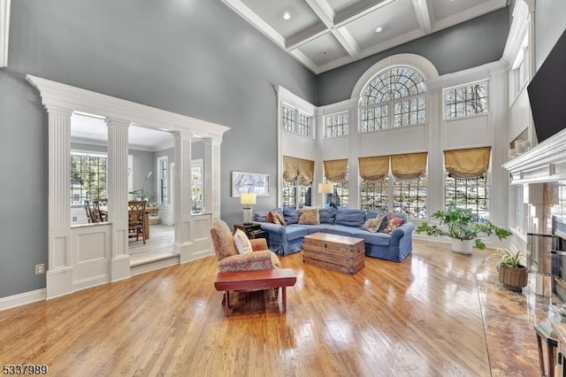 living area with coffered ceiling, a high ceiling, wood finished floors, and ornate columns