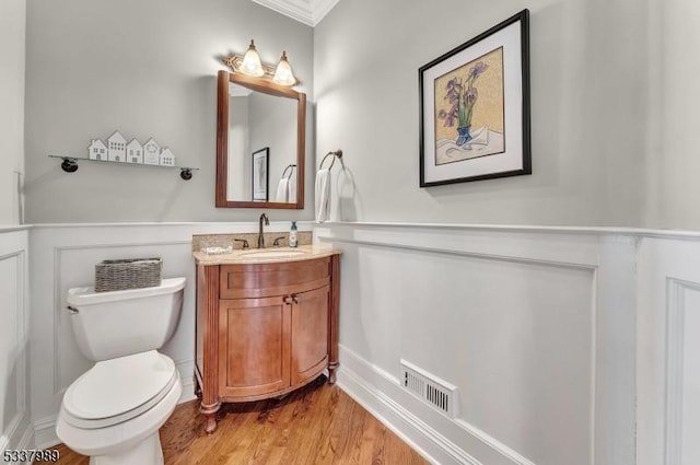 half bathroom featuring vanity, wood finished floors, a wainscoted wall, visible vents, and toilet