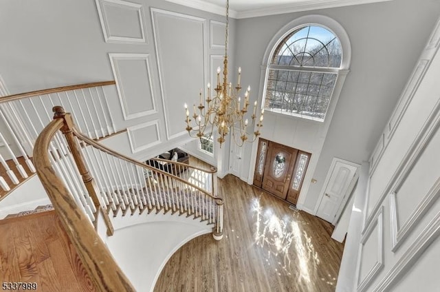 foyer entrance with a towering ceiling, ornamental molding, an inviting chandelier, and wood finished floors