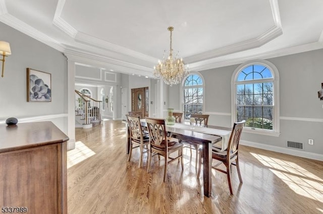 dining area with visible vents, stairs, light wood-style floors, and a tray ceiling