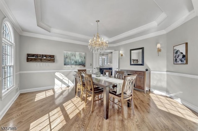 dining space with a wealth of natural light, a notable chandelier, light wood finished floors, and a tray ceiling