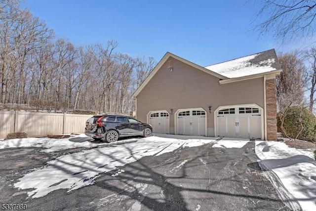 view of snowy exterior featuring a garage and fence