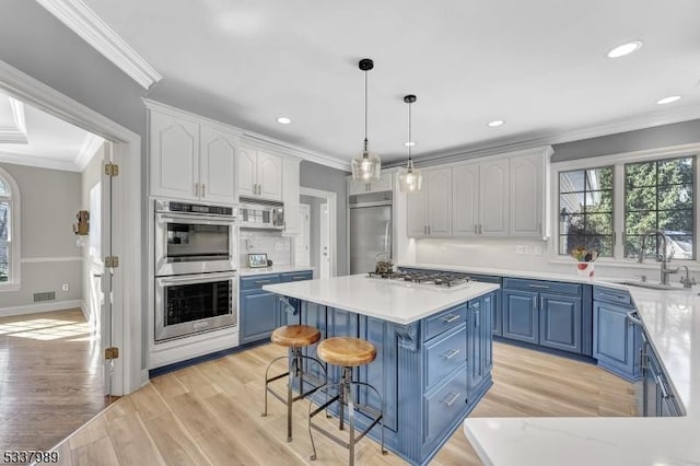 kitchen featuring blue cabinetry, ornamental molding, stainless steel appliances, and a sink