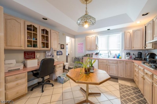 kitchen with built in desk, light brown cabinets, a raised ceiling, and pendant lighting