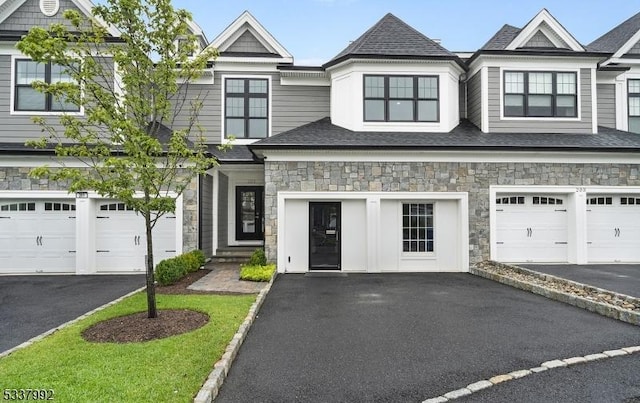 townhome / multi-family property with stone siding, a shingled roof, and driveway