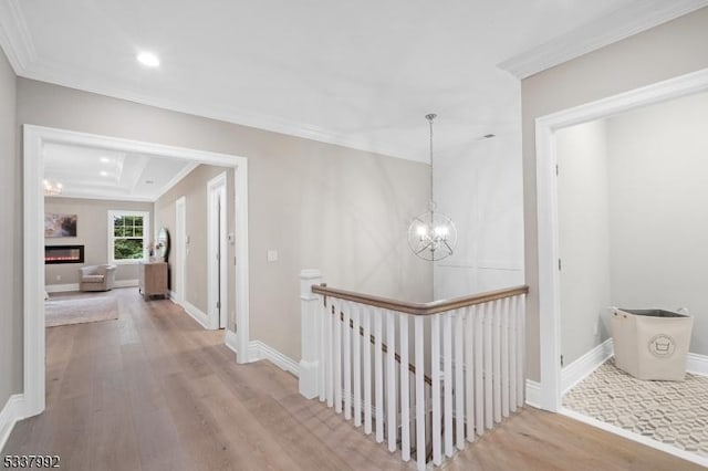 hallway featuring light wood-style flooring, a notable chandelier, an upstairs landing, baseboards, and ornamental molding