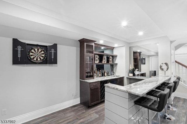 kitchen featuring light stone counters, a breakfast bar area, dark wood-type flooring, dark brown cabinets, and a peninsula