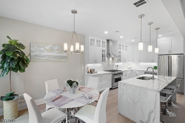 kitchen featuring stainless steel appliances, white cabinets, a center island with sink, and wall chimney range hood