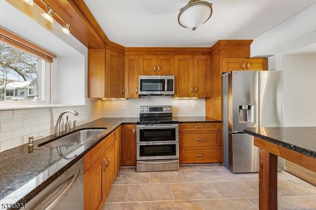 kitchen with stainless steel appliances, sink, decorative backsplash, and dark stone countertops