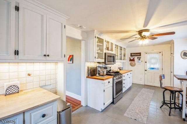 kitchen featuring butcher block counters, backsplash, white cabinets, ceiling fan, and stainless steel appliances