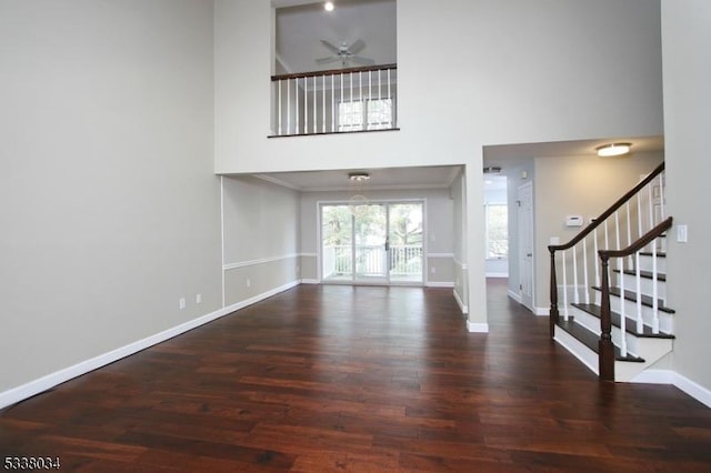 unfurnished living room with ceiling fan, dark wood-type flooring, and a high ceiling