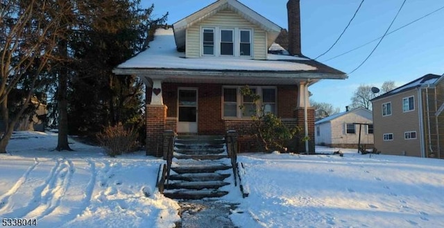 view of front of home with a porch, brick siding, and a chimney