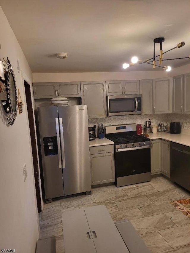 kitchen with gray cabinetry, backsplash, decorative light fixtures, and stainless steel appliances