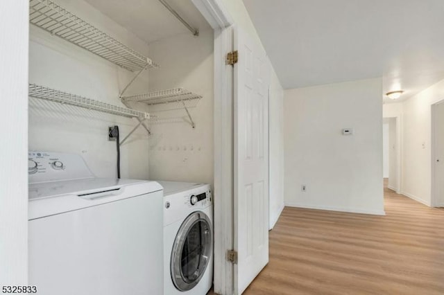 clothes washing area with light wood-type flooring, baseboards, washing machine and dryer, and laundry area