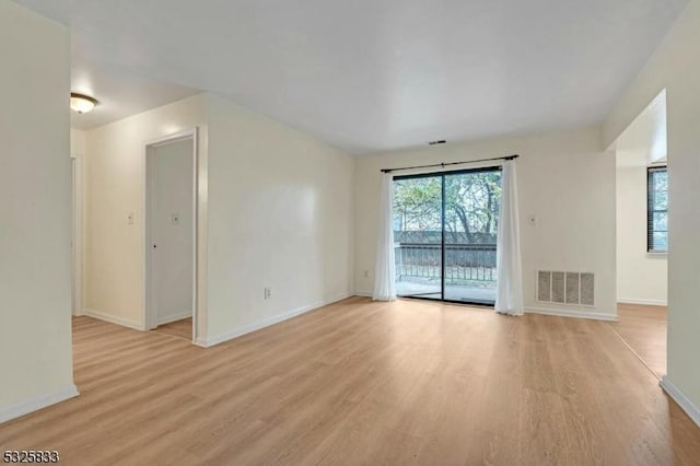 empty room featuring a wealth of natural light, visible vents, baseboards, and light wood finished floors