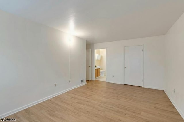 unfurnished bedroom featuring light wood-style floors, baseboards, and ensuite bathroom