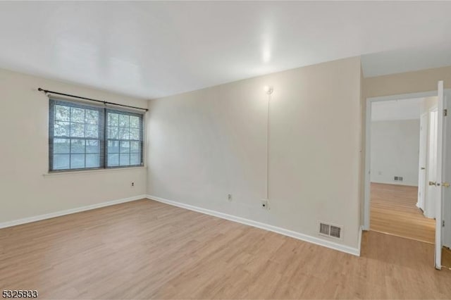 empty room featuring visible vents, light wood-type flooring, and baseboards