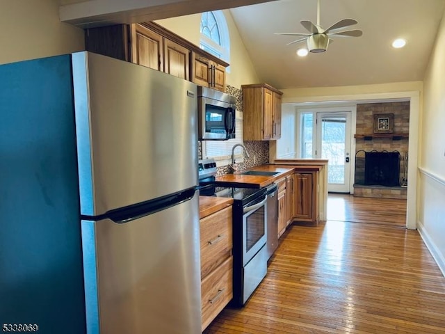 kitchen featuring appliances with stainless steel finishes, a fireplace, lofted ceiling, backsplash, and light hardwood / wood-style flooring