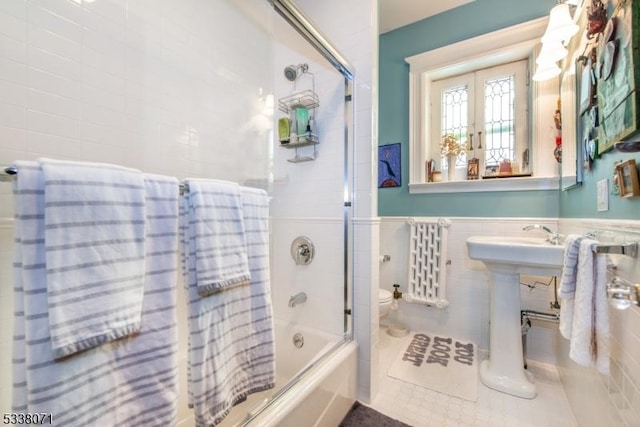 bathroom with tile patterned floors, toilet, combined bath / shower with glass door, tile walls, and radiator