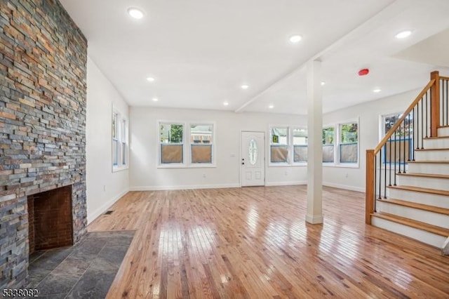 unfurnished living room with hardwood / wood-style flooring, a stone fireplace, and a wealth of natural light