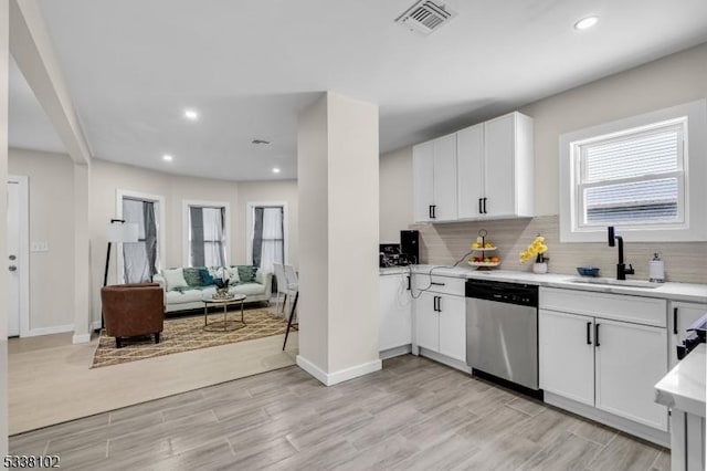 kitchen with sink, white cabinetry, backsplash, stainless steel dishwasher, and light wood-type flooring